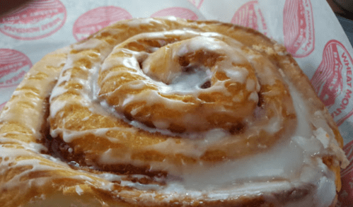 Close-up of a cinnamon roll drizzled with icing, resting on a red and white patterned paper.