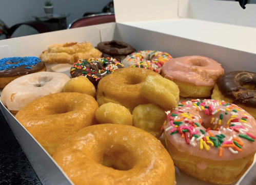 A box filled with various donuts, including glazed, chocolate, and sprinkled varieties, arranged neatly.