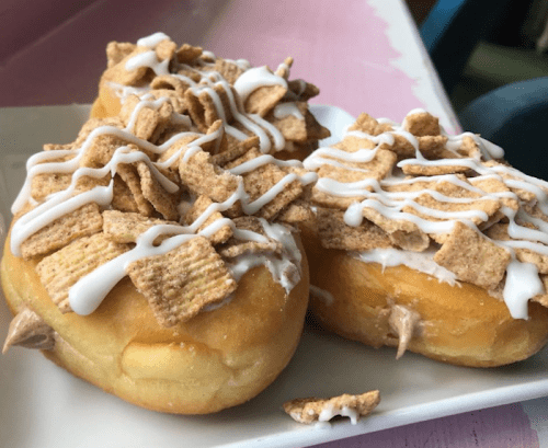 Two donuts topped with icing and crunchy cereal pieces, served on a white plate.