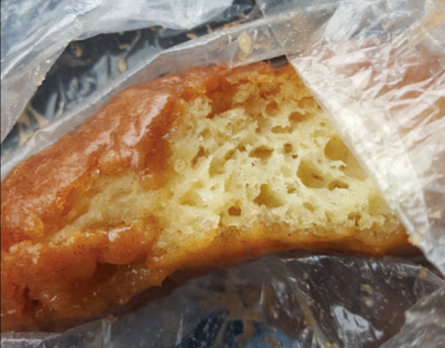 Close-up of a partially eaten sweet pastry, showing a golden-brown exterior and a soft, airy interior.
