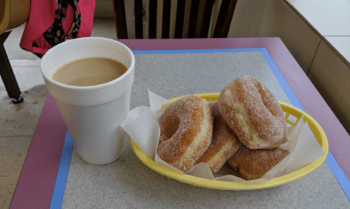 A yellow basket with four donuts and a large cup of coffee on a table.