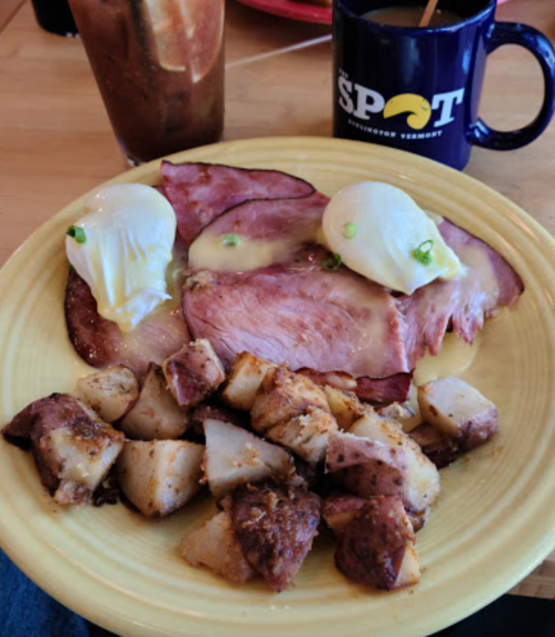A plate of ham with two poached eggs and seasoned potatoes, accompanied by a coffee mug.