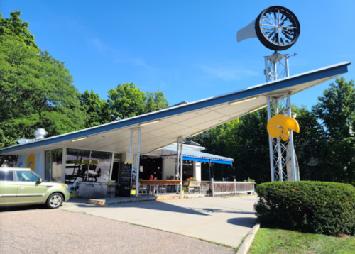 A retro-style diner with a large turbine sculpture on the roof, surrounded by trees and a parking area.
