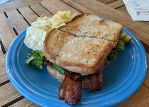 A sandwich with bacon and lettuce on whole grain bread, served with a side of potato chips on a blue plate.