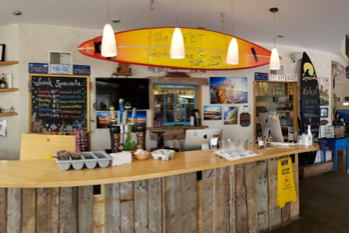 A beach-themed bar with a wooden counter, surfboard decor, chalkboard menus, and modern equipment in a bright setting.