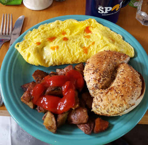 A plate with a yellow omelet, seasoned potatoes with ketchup, and a toasted bagel on a blue dish.