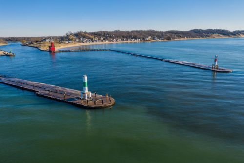 Aerial view of a calm waterway with piers and colorful buoys, surrounded by a shoreline and clear blue sky.