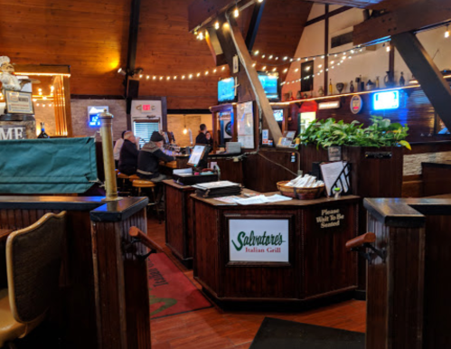 Interior of an Italian restaurant with wooden decor, tables, and a welcoming atmosphere. Soft lighting and patrons visible.