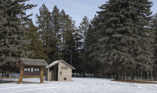 A small building and information sign surrounded by snow-covered ground and tall evergreen trees.