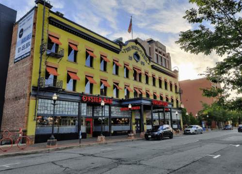 Historic yellow building with orange awnings, featuring an oyster bar and outdoor seating, on a city street.