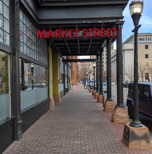 A view of Market Street with a red sign, lined with lampposts and brick pavement, leading to buildings in the background.