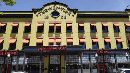 Historic yellow building with orange awnings, featuring "Fresh Fish" and "Grill" signage, under a clear blue sky.