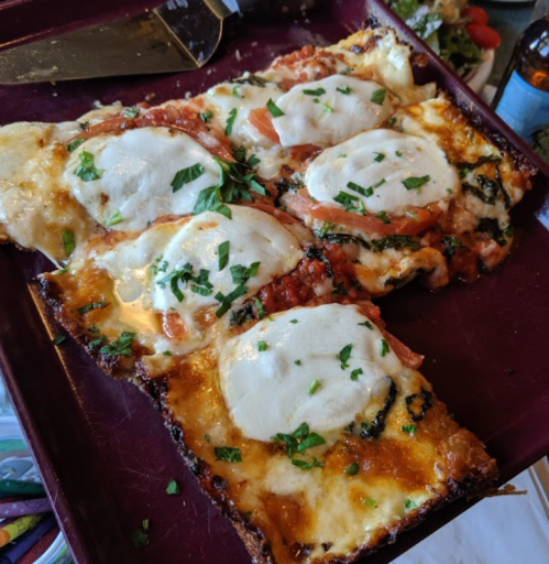 A tray of freshly baked pizza with melted mozzarella, tomato slices, and chopped herbs on top.