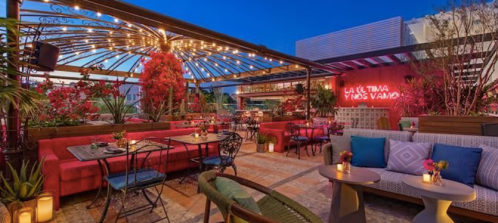 Rooftop restaurant with vibrant decor, cozy seating, and string lights, set against a twilight sky.