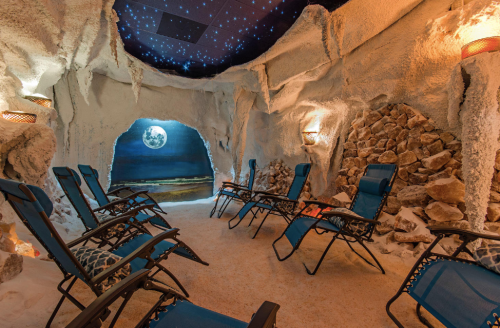 A serene salt therapy room with reclining chairs, rock walls, and a starry ceiling, creating a calming atmosphere.