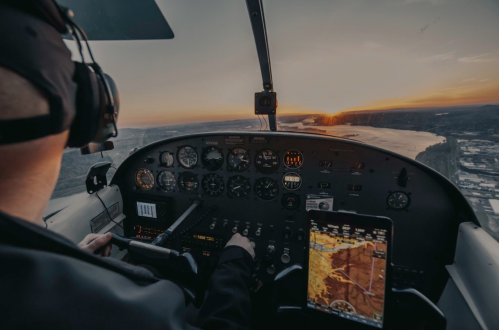 Pilot in cockpit at sunset, navigating with instruments and a tablet displaying a map over a river landscape.