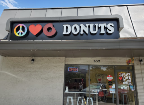 Sign for a donut shop featuring a peace symbol, heart, and donut icon, with an "OPEN" sign in the window.