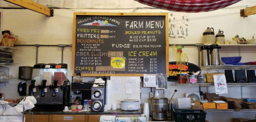 A farm stand menu board listing items like fried pies, cider slushy, fudge, ice cream, and coffee with prices.