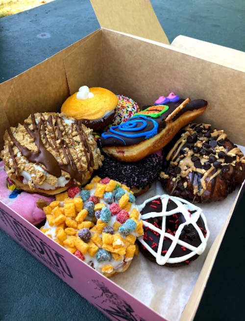 A box filled with colorful, decorated donuts, including chocolate, sprinkles, and cereal toppings.