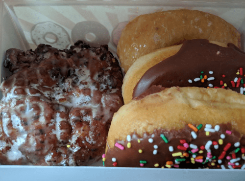 A box of assorted donuts, including a chocolate-glazed donut with sprinkles and a glazed donut.
