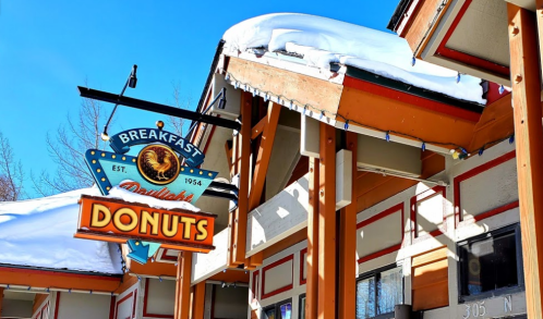 A colorful sign reading "Breakfast Donuts" hangs from a building with snow-covered roofs under a clear blue sky.