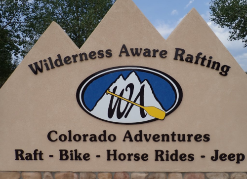 Sign for Wilderness Aware Rafting featuring mountains and an oar, promoting Colorado adventures like rafting and biking.