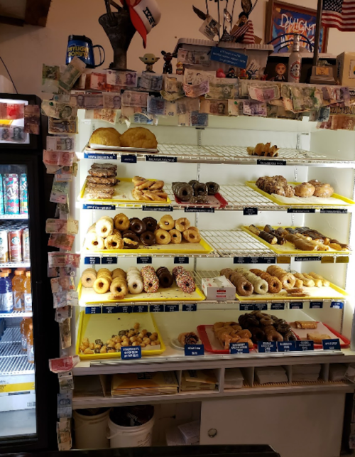 A display case filled with various donuts and pastries, decorated with dollar bills on the surrounding wall.