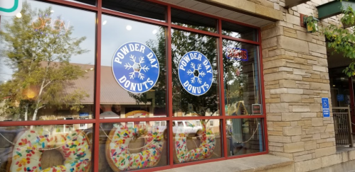 Exterior of a donut shop with large windows displaying colorful donuts and the sign "Pounder Day Donuts."