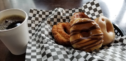A plate with four donuts and a cup of coffee, all on a checkered paper napkin.