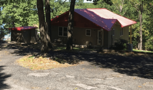 A house with a red roof surrounded by trees, located on a winding driveway.