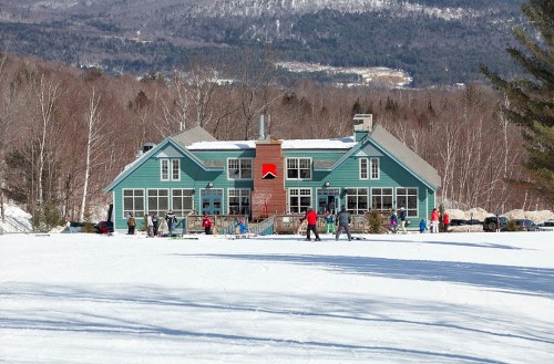 A blue ski lodge surrounded by snow, with people skiing and enjoying the winter scenery in the background.