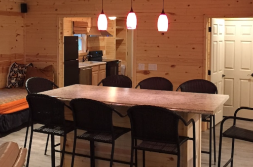 Cozy wooden interior of a cabin featuring a kitchen, dining table, and seating area with modern lighting.