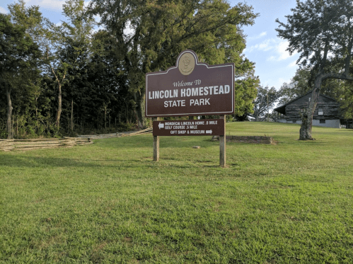 Sign for Lincoln Homestead State Park, featuring park name and information about nearby attractions, set in a grassy area.