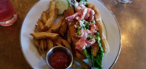 A plate featuring a lobster roll with lettuce and a side of crispy fries, accompanied by a small cup of ketchup.