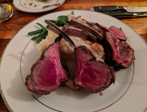 A plate featuring three lamb chops, mashed potatoes, and green beans, presented elegantly on a wooden table.