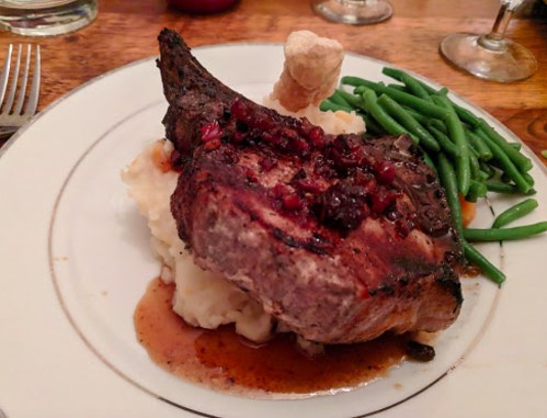 A plate featuring a grilled pork chop with a savory sauce, mashed potatoes, and green beans on the side.