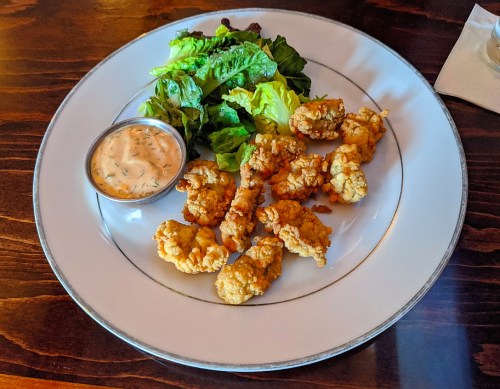 A plate of fried shrimp with a side of lettuce and a small cup of dipping sauce.