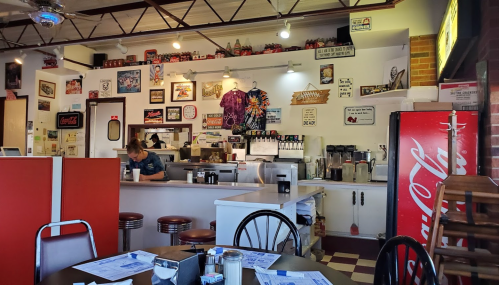 A cozy diner interior with a counter, vintage decor, and a Coca-Cola fridge, featuring a staff member at work.