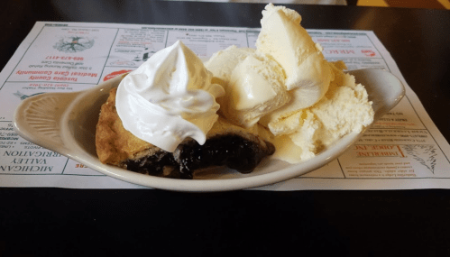 A dish featuring warm blueberry pie with a scoop of vanilla ice cream and whipped cream, served on a plate.