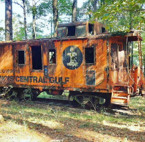 An old, rusted caboose with the number 3, surrounded by trees in a wooded area.