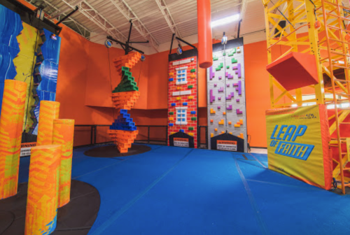 Indoor adventure park featuring colorful climbing walls, foam pillars, and a "Leap of Faith" challenge area.