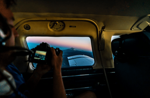 A person in a small plane captures a photo of a mountain at sunset through the window.