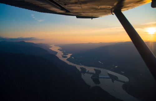 Aerial view of a winding river at sunset, with mountains and a bridge visible in the distance.