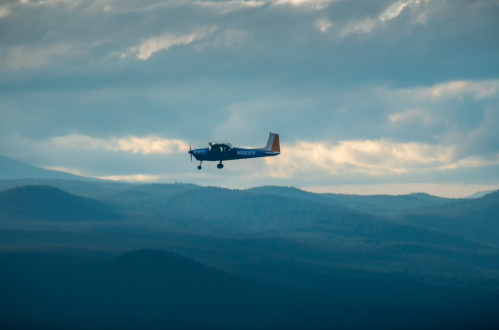 A small airplane flying over a mountainous landscape under a cloudy sky.