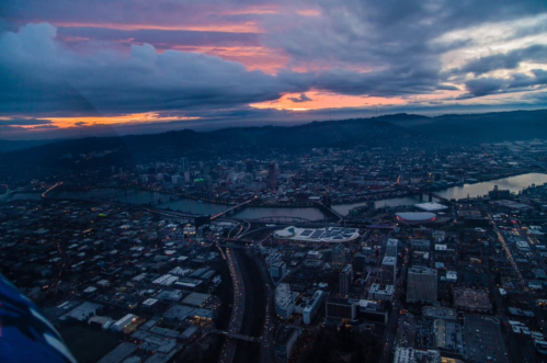 Aerial view of a city at sunset, with rivers, buildings, and dramatic clouds in the sky.