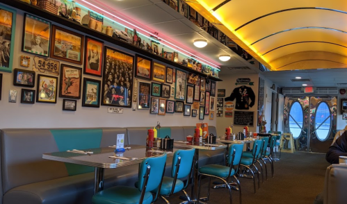 A retro diner interior with teal chairs, a curved ceiling, and walls adorned with vintage photos and memorabilia.