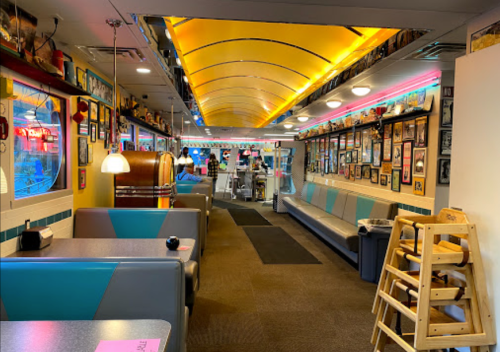 A colorful diner interior with booths, a jukebox, and walls adorned with framed photos and memorabilia.