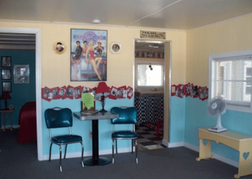 A retro-style room with blue and yellow walls, featuring a table with two chairs, a fan, and vintage decor.