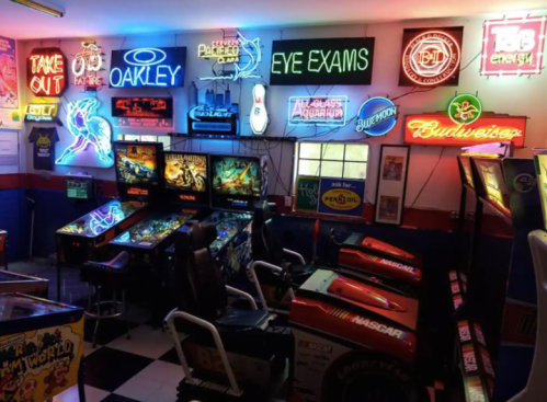 A vibrant arcade with neon signs, pinball machines, and racing games in a retro-style room.
