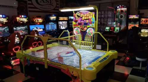 A brightly colored Pac-Man arcade game surrounded by various other arcade machines in a gaming venue.